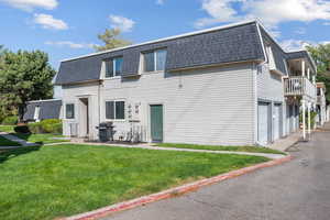 Rear view of house with roof with shingles, mansard roof, a yard, a balcony, and an attached garage