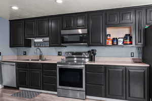 Kitchen featuring dark cabinets, appliances with stainless steel finishes, light countertops, light wood-style floors, and recessed lighting