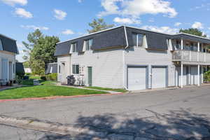 View of side of home featuring mansard roof, a shingled roof, a lawn, a balcony, and a garage