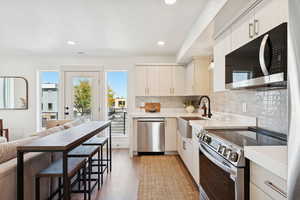 Kitchen featuring appliances with stainless steel finishes, backsplash, light wood-style flooring, recessed lighting, and light stone counters