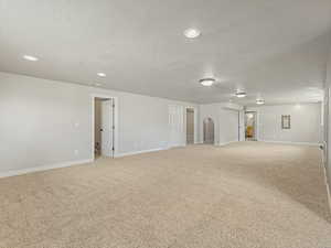 Unfurnished room with light colored carpet, a textured ceiling, arched walkways, and recessed lighting