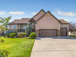 Craftsman-style home featuring stone siding, a front lawn, driveway, and board and batten siding