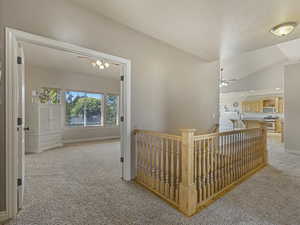 Corridor featuring an upstairs landing, light colored carpet, and vaulted ceiling