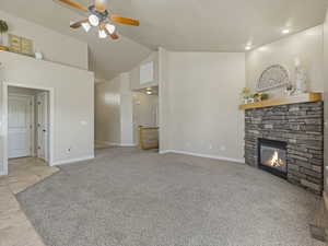 Unfurnished living room with a stone fireplace, ceiling fan, light colored carpet, light tile patterned flooring, and high vaulted ceiling