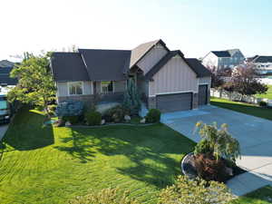 View of front facade with board and batten siding, a front yard, stone siding, driveway, and a garage