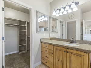Full bath with a spacious closet, vanity, and light carpet