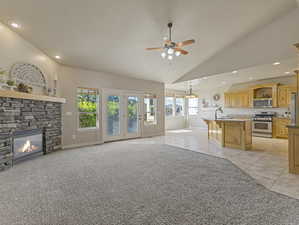 Unfurnished living room featuring light colored carpet, a stone fireplace, light tile patterned floors, ceiling fan, and recessed lighting