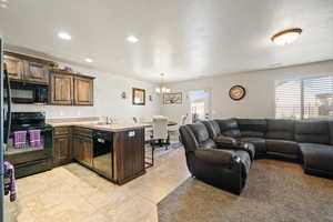 Kitchen featuring a kitchen bar, black appliances, dark brown cabinets, a peninsula, and light countertops