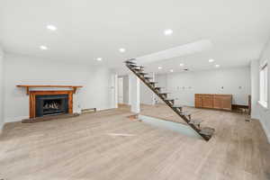 Unfurnished living room with recessed lighting, a fireplace with raised hearth, stairway, and light wood-style flooring