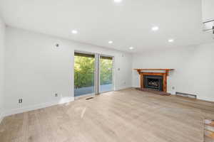 Unfurnished living room with recessed lighting, a fireplace with raised hearth, and light wood-style flooring
