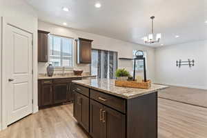 Kitchen featuring dark brown cabinets, light stone counters, decorative light fixtures, recessed lighting, and a center island