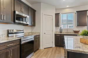 Kitchen featuring stainless steel appliances, light wood finished floors, dark brown cabinetry, light stone countertops, and recessed lighting
