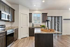Kitchen featuring appliances with stainless steel finishes, dark brown cabinets, light stone counters, light wood finished floors, and recessed lighting