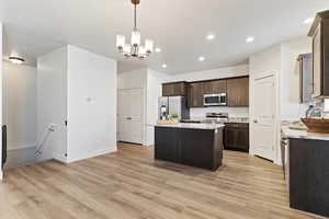 Kitchen featuring pendant lighting, dark brown cabinetry, stainless steel appliances, a kitchen island, and light wood-type flooring