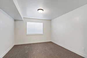 Unfurnished room featuring dark colored carpet and a textured ceiling