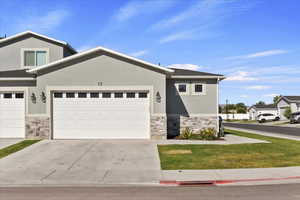 View of front of property with stone siding, concrete driveway, stucco siding, and a front lawn
