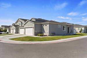 View of front of property with stone siding, concrete driveway, a front yard, stucco siding, and a garage