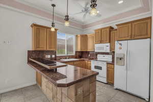 Kitchen with white appliances, decorative backsplash, decorative light fixtures, dark countertops, and a tray ceiling