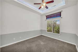Empty room featuring a tray ceiling, carpet, and ceiling fan