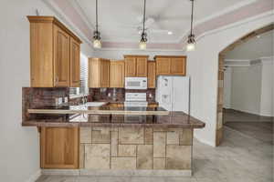 Kitchen with arched walkways, decorative backsplash, white appliances, pendant lighting, and a peninsula