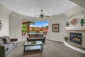 Living area featuring carpet flooring, a tiled fireplace, and ceiling fan