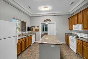 Kitchen with white appliances, light stone counters, brown cabinets, a kitchen island, and a raised ceiling