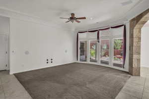 Spare room featuring light tile patterned floors, light carpet, ceiling fan, and crown molding