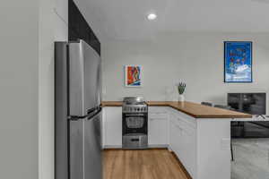 Kitchen with freestanding refrigerator, electric stove, white cabinetry, light wood-style flooring, and a peninsula