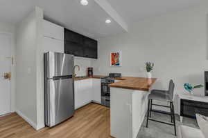 Kitchen with butcher block counters, freestanding refrigerator, a peninsula, a breakfast bar, and recessed lighting