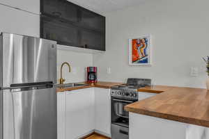 Kitchen featuring freestanding refrigerator, freestanding range oven, butcher block countertops, white cabinetry, and glass insert cabinets