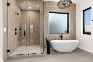 Bathroom with a shower stall, a soaking tub, hanging lights, light tile patterned floors, and tile walls