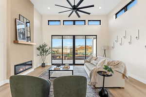 Living area with light wood-style floors, healthy amount of natural light, a glass covered fireplace, recessed lighting, and a ceiling fan