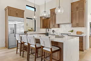 Kitchen with a kitchen bar, light stone counters, built in fridge, wood finish cabinets, and hanging light fixtures