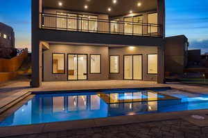 Back of property at dusk with a patio area, a pool with connected hot tub, and stucco siding