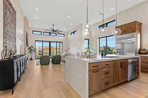 Kitchen with open floor plan, wood finish cabinetry, a center island with sink, light stone counters, and a high ceiling