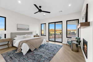 Bedroom featuring access to exterior, light wood finished floors, a glass covered fireplace, a ceiling fan, and recessed lighting