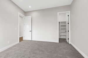 Unfurnished bedroom with a walk in closet, dark colored carpet, and recessed lighting