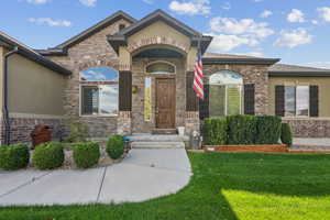 View of exterior entry featuring a lawn, brick siding, stucco siding, and stone siding
