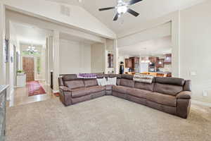Living area with a chandelier, light carpet, a ceiling fan, and lofted ceiling