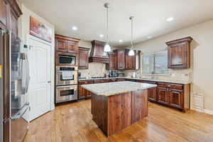 Kitchen with stainless steel appliances, decorative backsplash, light wood-style flooring, light stone countertops, and recessed lighting