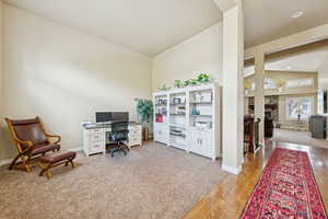Home office with a fireplace, light wood-style floors, light carpet, and lofted ceiling