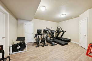 Workout room with light wood-style flooring and a textured ceiling