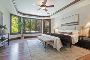 Bedroom featuring crown molding, wood finished floors, a raised ceiling, and a ceiling fan