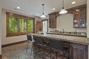 Kitchen featuring a breakfast bar, glass insert cabinets, hanging light fixtures, recessed lighting, and dark stone counters