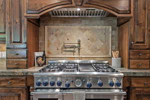 Kitchen view of pot filler, double oven range, decorative backsplash, and custom range hood