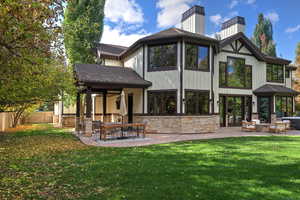 Back of house featuring a patio, roof with shingles, a chimney, and stone siding