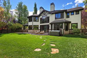 Back of house featuring a sunroom, a chimney, stone siding, and a patio area