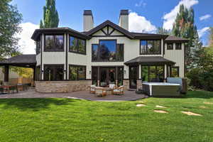 Rear view of house with a chimney, a patio, a lawn, and stone siding