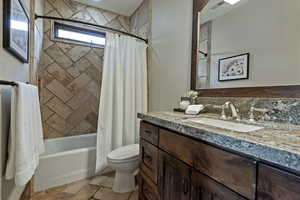 Full bath with shower / bath combo, vanity, and stone tile floors