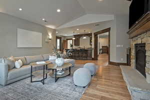 Living area featuring light wood-style floors, lofted ceiling, a stone fireplace, and recessed lighting
